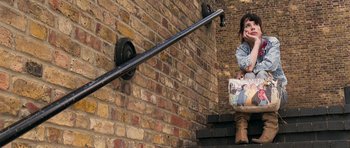 Movie still from “Happy-Go-Lucky” (2008), directed by Mike Leigh – A child sitting on a step with a newspaper in hand; Medium shot, High angle