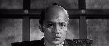 Movie still from “Harakiri” (1962), directed by Masaki Kobayashi – A black and white photo of a man with a shaved head; Close Up shot, Over the shoulder angle