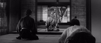 Movie still from “Harakiri” (1962), directed by Masaki Kobayashi – A man sitting on the ground in front of a tree; Wide shot, Over the shoulder angle