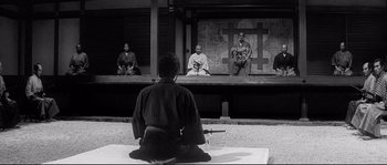 Movie still from “Harakiri” (1962), directed by Masaki Kobayashi – A man sitting on the ground in front of a group of people; Wide shot, Over the shoulder angle