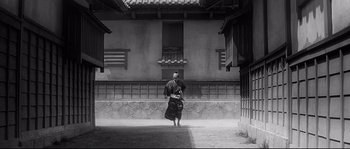 Movie still from “Harakiri” (1962), directed by Masaki Kobayashi – A man walking in a courtyard with a building in the background; Extreme Wide shot, Low angle