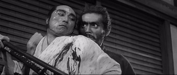 Movie still from “Harakiri” (1962), directed by Masaki Kobayashi – A man holding another man's arm in front of a building; Medium shot, Low angle