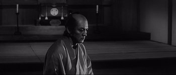 Movie still from “Harakiri” (1962), directed by Masaki Kobayashi – A man with a shaved head is standing in front of a clock; Medium shot, Low angle
