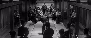 Movie still from “Harakiri” (1962), directed by Masaki Kobayashi – A group of people sitting in a room with a man standing in front of them; Wide shot, High angle