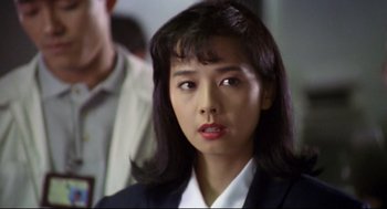 Movie still from “Hard Boiled” (1992), directed by John Woo – A woman in a black suit and red lipstick; Close Up shot, Over the shoulder angle