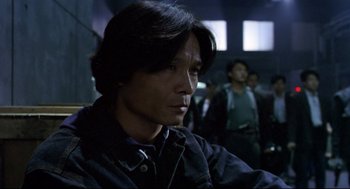 Movie still from “Hard Boiled” (1992), directed by John Woo – A man with long black hair is looking to his left; Close Up shot, Low angle