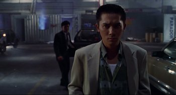 Movie still from “Hard Boiled” (1992), directed by John Woo – A man in a suit standing in front of another man in a suit; Medium shot, Low angle