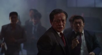 Movie still from “Hard Boiled” (1992), directed by John Woo – An older man wearing a suit and tie; Medium shot, Low angle