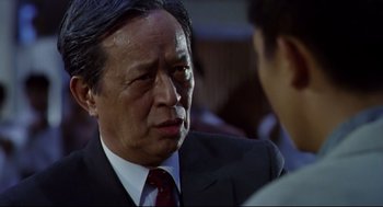 Movie still from “Hard Boiled” (1992), directed by John Woo – An older man in a suit and a tie; Close Up shot, Over the shoulder angle