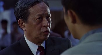 Movie still from “Hard Boiled” (1992), directed by John Woo – An older man in a suit and tie talking to a young man; Close Up shot, Over the shoulder angle
