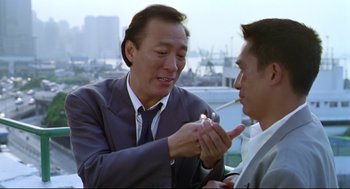Movie still from “Hard Boiled” (1992), directed by John Woo – A man in a suit lighting a cigarette with another man in a suit; Medium shot, Low angle