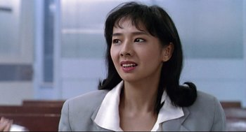 Movie still from “Hard Boiled” (1992), directed by John Woo – A woman in a gray jacket and white shirt; Close Up shot, High angle