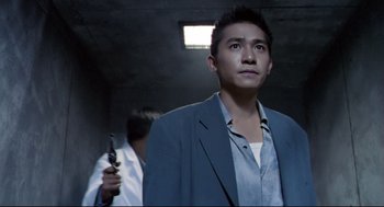 Movie still from “Hard Boiled” (1992), directed by John Woo – A man holding a gun while standing next to another man; Medium shot, Low angle