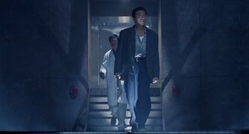 Movie still from “Hard Boiled” (1992), directed by John Woo – A man walking down a flight of stairs while another man walks up the stairs; Wide shot, Low angle