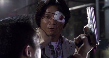 Movie still from “Hard Boiled” (1992), directed by John Woo – A man with a fake eye patch on his face; Close Up shot, Low angle
