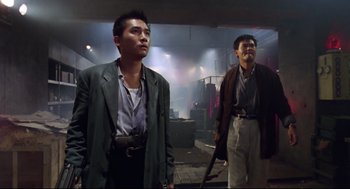Movie still from “Hard Boiled” (1992), directed by John Woo – Two asian men in suits stand in an industrial setting; Medium shot, Low angle