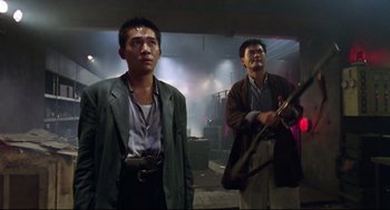 Movie still from “Hard Boiled” (1992), directed by John Woo – Two men in suits and ties are standing in a dark room; Medium shot, Low angle