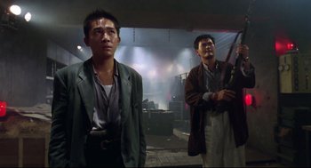 Movie still from “Hard Boiled” (1992), directed by John Woo – Two asian men standing next to each other in a dark room; Medium shot, Low angle