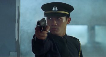 Movie still from “Hard Boiled” (1992), directed by John Woo – A man in a uniform holding a gun pointed at the camera; Medium shot, Low angle