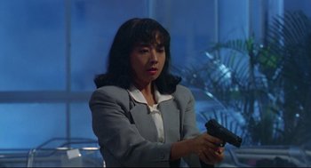 Movie still from “Hard Boiled” (1992), directed by John Woo – A woman in a suit holding a gun in her hand; Medium shot, Low angle