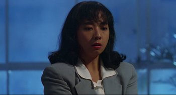 Movie still from “Hard Boiled” (1992), directed by John Woo – A woman with long hair wearing a gray jacket; Close Up shot, Low angle