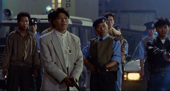 Movie still from “Hard Boiled” (1992), directed by John Woo – A group of men standing next to each other on a street; Medium shot, Low angle