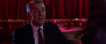 Movie still from “Hard Eight” (1996), directed by Paul Thomas Anderson – An older man wearing a suit and tie in front of a red background; Close Up shot, Low angle
