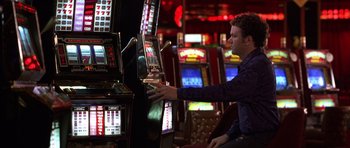 Movie still from “Hard Eight” (1996), directed by Paul Thomas Anderson – A man sitting in front of a row of slot machines; Medium shot, Over the shoulder angle