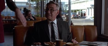 Movie still from “Hard Eight” (1996), directed by Paul Thomas Anderson – A man in a suit and tie sitting in front of a plate of food; Medium shot, Over the shoulder angle