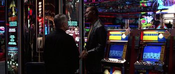 Movie still from “Hard Eight” (1996), directed by Paul Thomas Anderson – Two men standing in front of slot machines in a casino; Medium shot, Over the shoulder angle