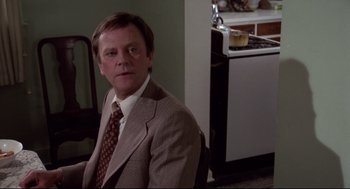 Movie still from “Hardcore” (1979), directed by Paul Schrader – A man wearing a suit and tie sitting in a chair; Medium shot, Over the shoulder angle