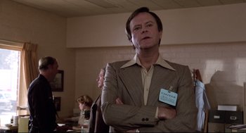 Movie still from “Hardcore” (1979), directed by Paul Schrader – A man in a brown suit with a name tag on his chest; Medium shot, Low angle