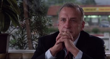 Movie still from “Hardcore” (1979), directed by Paul Schrader – A man in a suit and tie sitting in front of a plant; Close Up shot, Over the shoulder angle