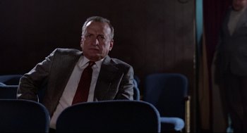 Movie still from “Hardcore” (1979), directed by Paul Schrader – A man in a suit and tie sitting in a chair in a room; Medium shot, Low angle