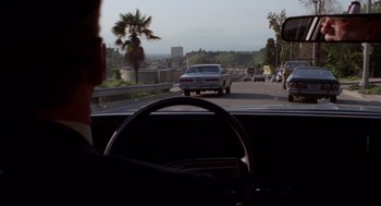 Movie still from “Hardcore” (1979), directed by Paul Schrader – A man driving a car on a street with a lot of traffic; Wide shot, Over the shoulder angle