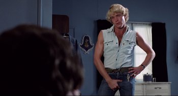 Movie still from “Hardcore” (1979), directed by Paul Schrader – A man in a white shirt and blue jeans is standing in front of a mirror; Medium shot, Over the shoulder angle