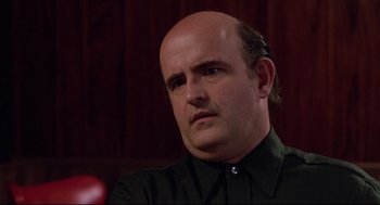 Movie still from “Hardcore” (1979), directed by Paul Schrader – A man with a bald head is sitting in a room; Close Up shot, Over the shoulder angle