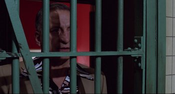 Movie still from “Hardcore” (1979), directed by Paul Schrader – A man behind a green metal fence looking at the camera; Medium shot, Low angle