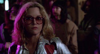 Movie still from “Hardcore” (1979), directed by Paul Schrader – A woman wearing glasses and a silver jacket with a heart on it; Close Up shot, Over the shoulder angle