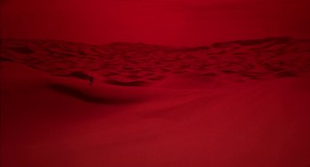 Movie still from “Hardware” (1990), directed by Richard Stanley – A person standing on top of a red sand dune; Extreme Wide shot, High angle