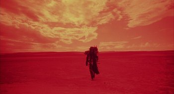 Movie still from “Hardware” (1990), directed by Richard Stanley – A man walking across a barren field under a cloudy sky; Extreme Wide shot, Low angle