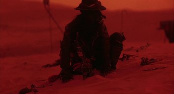 Movie still from “Hardware” (1990), directed by Richard Stanley – A man in a hat and a jacket sitting in the snow; Wide shot, Low angle