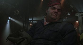 Movie still from “Hardware” (1990), directed by Richard Stanley – A man with a red hat is sitting in a dark room; Close Up shot, Low angle