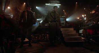 Movie still from “Hardware” (1990), directed by Richard Stanley – Two men standing next to each other in a dark room; Wide shot, Low angle
