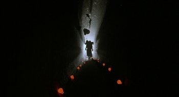 Movie still from “Hardware” (1990), directed by Richard Stanley – A person standing in a dark tunnel with lights; Extreme Wide shot, Low angle