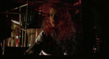 Movie still from “Hardware” (1990), directed by Richard Stanley – A woman with curly red hair is sitting in a dark room; Close Up shot, Low angle