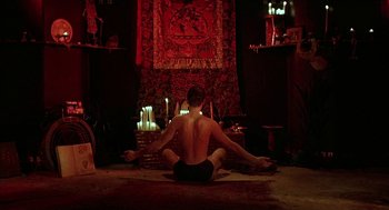 Movie still from “Hardware” (1990), directed by Richard Stanley – A man sitting on the ground in front of candles; Wide shot, High angle