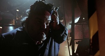 Movie still from “Hardware” (1990), directed by Richard Stanley – A man in a black shirt is holding a cell phone; Close Up shot, Low angle