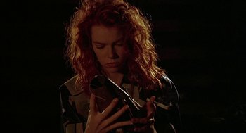 Movie still from “Hardware” (1990), directed by Richard Stanley – A woman with long red curly hair holding a violin; Close Up shot, Low angle