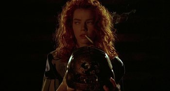 Movie still from “Hardware” (1990), directed by Richard Stanley – A woman smoking a cigarette while holding a helmet; Close Up shot, Low angle
